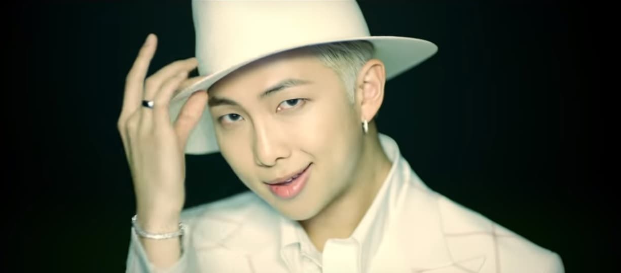 RM, quien toma el papel de rapero en BTS, usa un sombrero fedora y atuendo rosa pastel.