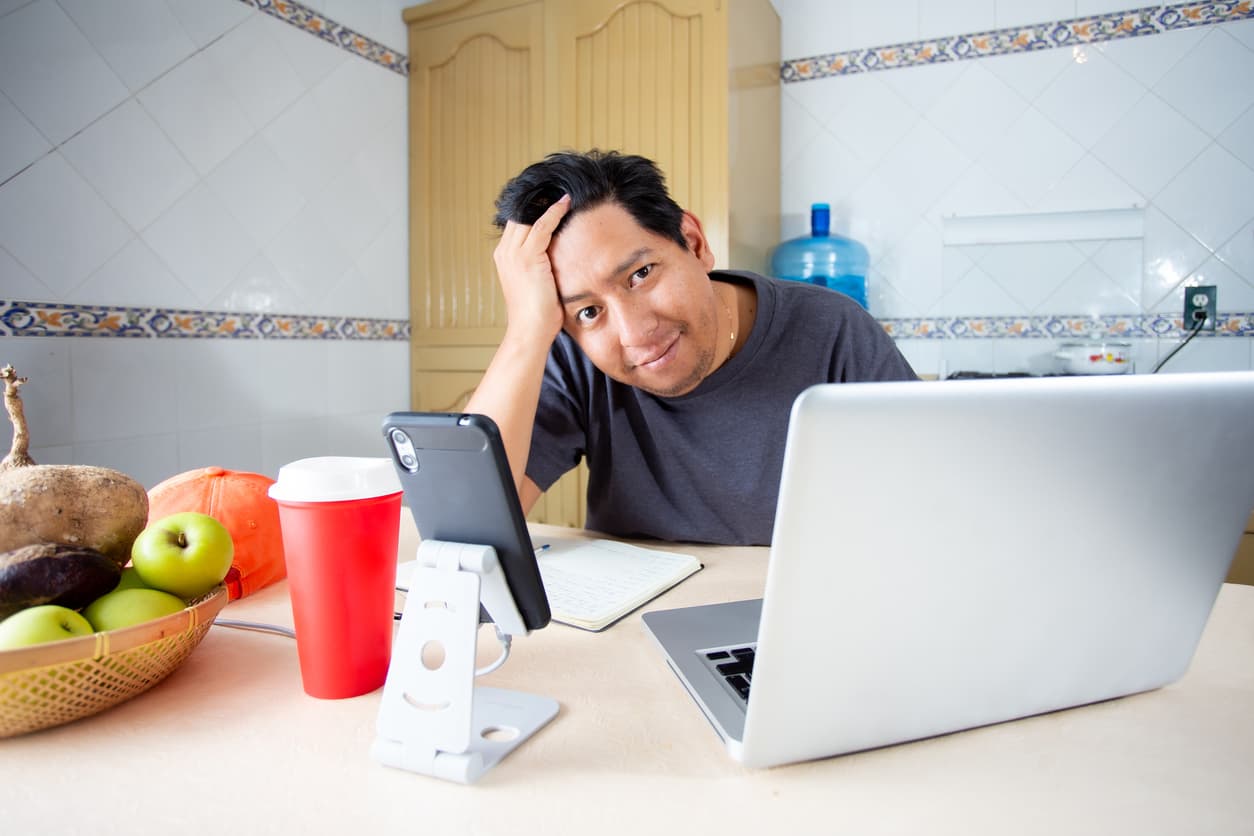 Man working from home with his laptop and cell phone, answering calls and being amazed by the contents of the computer.
