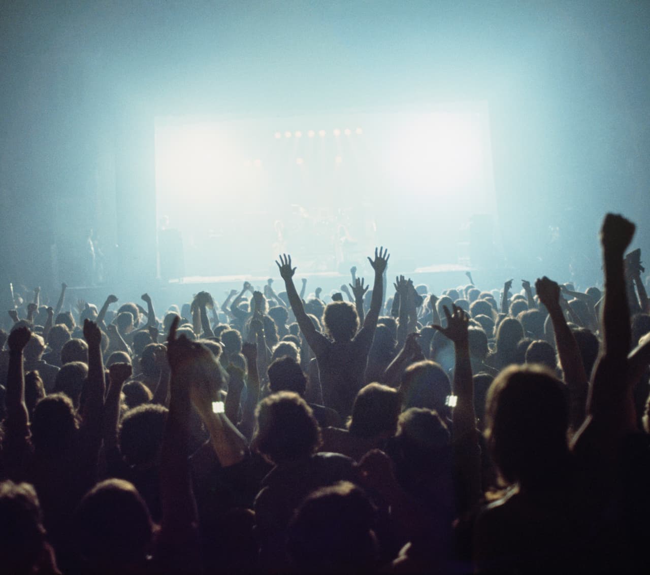 A view of the crowds of fans during the encore finale of a rock concert from the back of a venue looking to a bightly lit stage over the heads and raised arms of a cheering audience, circa 1980. (Photo by Fin Costello/Redferns)