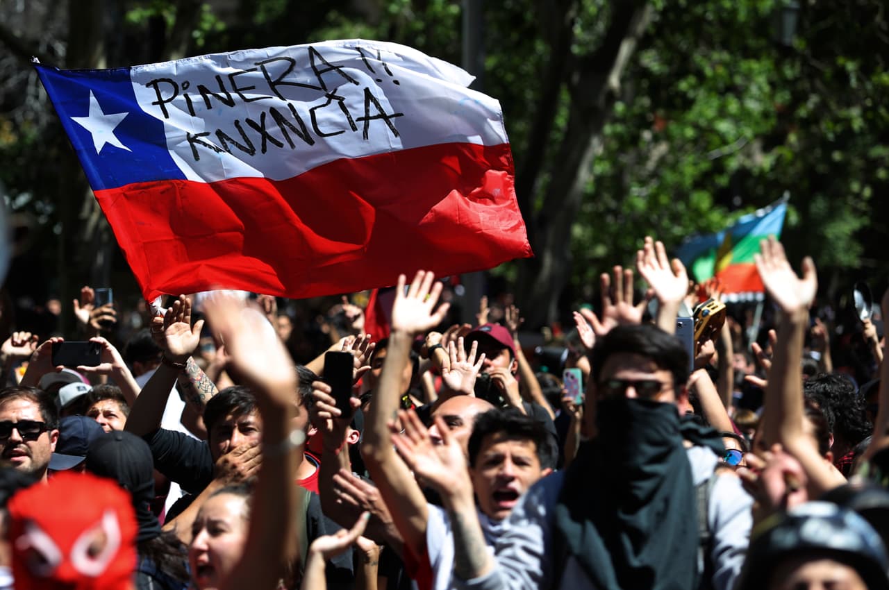 Protesters wave a Chilean flag, marked with a message that reads in Spanish: "Pinera quit" during a demonstration in Santiago, Chile, Monday, Oct. 21, 2019. Although the Chilean capital seemed to return to calm on Monday after three days of protests that led President Sebastian Pinera to say that the country is “at war” against a powerful enemy. (AP Photo/Miguel Arenas)
