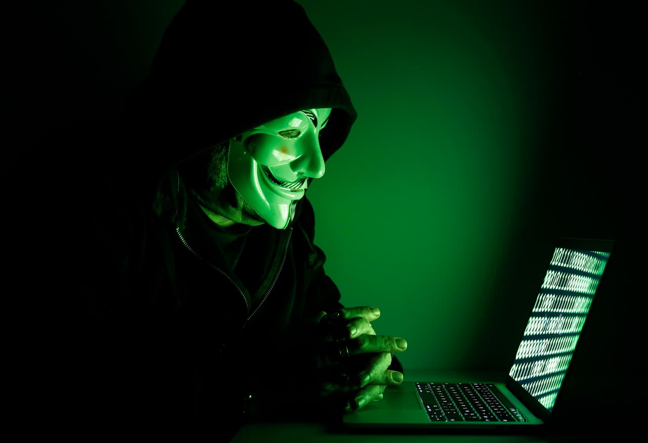 PARIS, FRANCE - DECEMBER 27: In this photo illustration, a hacker with an Anonymous mask on his face and a hood on his head uses a computer on December 27, 2019 in Paris, France. In IT security, a hacker is an IT specialist, who is looking for ways to bypass software and hardware protections. Hackers are generally intelligent programmers who seek to manipulate or modify a computer system or network. (Photo by Chesnot/Getty Images)