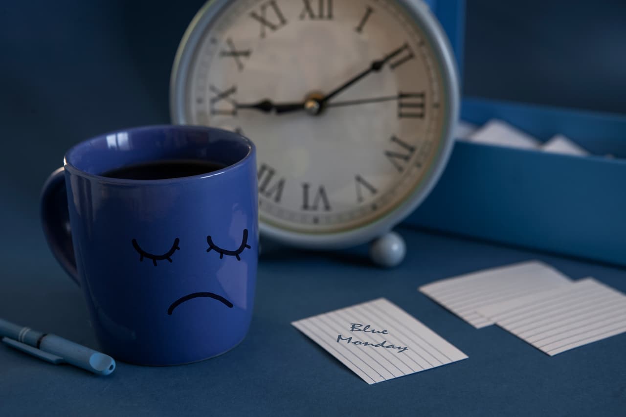 The beginning of the working day on blue Monday. Cup of tea, alarm clock and a note with the text Blue Monday. The most depressed day of the year
