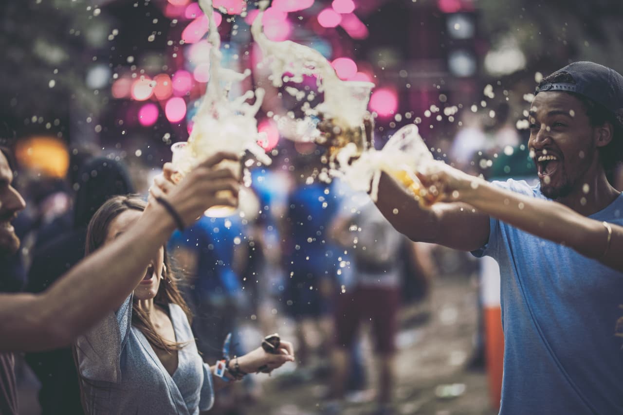 Group of happy friends having fun while toasting with beer and splashing it on a music festival.