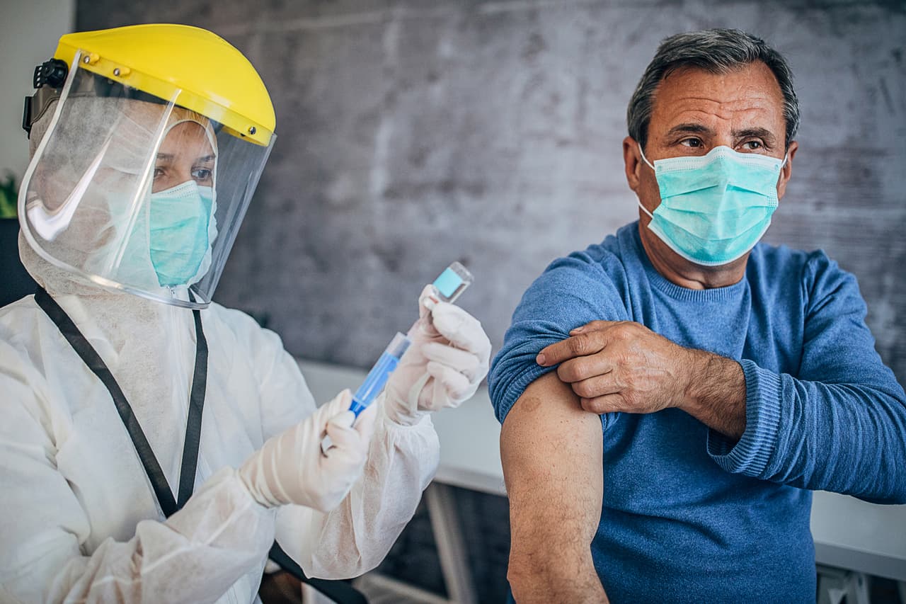 Two people, medical doctor in protective suit giving a senior male Covid-19 coronavirus vaccine.