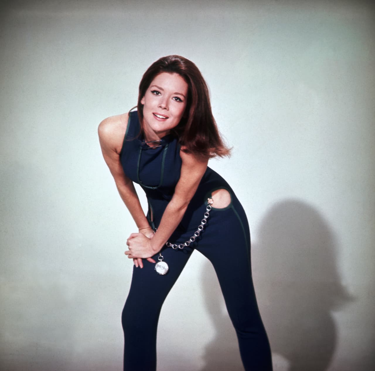 (Original Caption) 3/4 Length pose of Diana Rigg as Emma Peel in The Avengers. In this shot, Rigg is wearing a blue, one piece pants suit with cut out hips and an oversized pocketwatch and chain. Undated color photograph circa 1968.